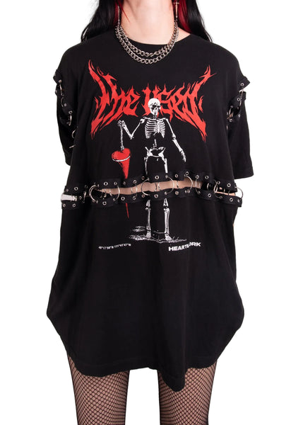 A person wearing an oversized black graphic T-shirt with a red and white skeleton print and distressed side details, paired with fishnet stockings and layered chain necklaces, against a plain light background. Indiefoxx Shop